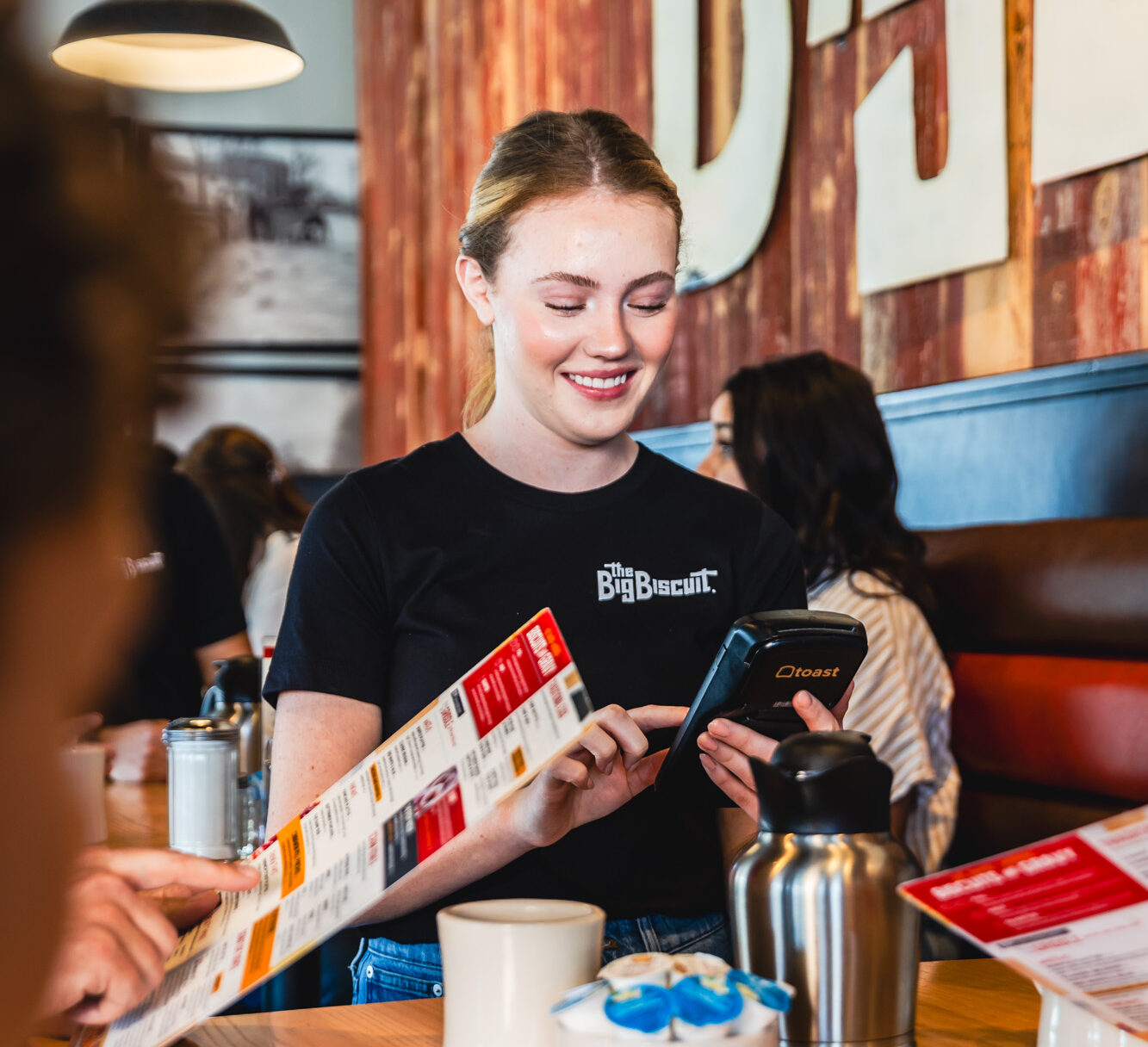 Woman in black shirt standing next to table, taking food order, smiling